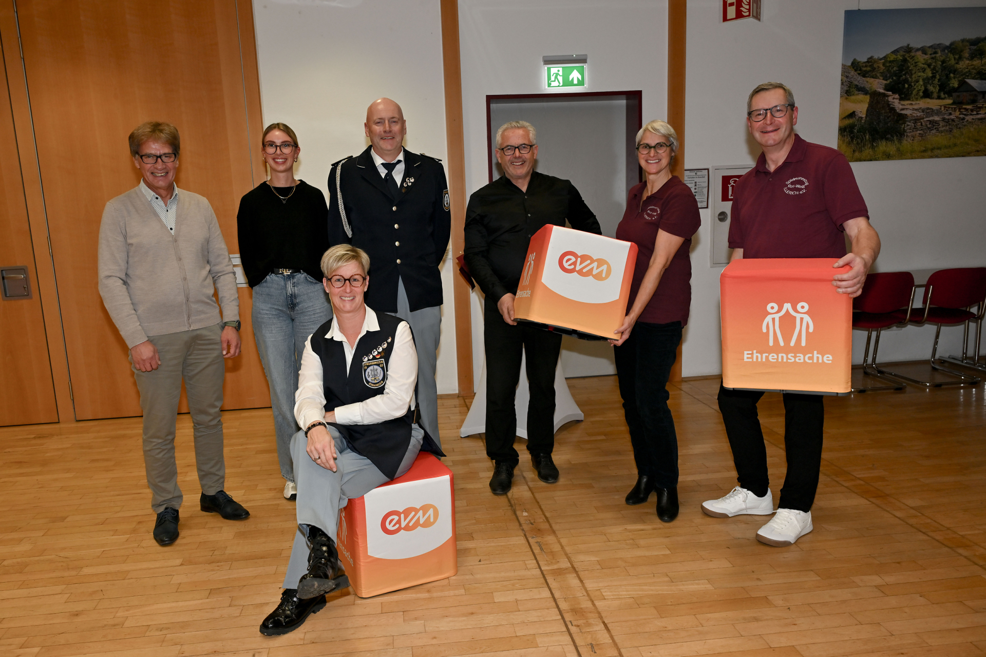 Gruppenfoto mit den Spielmannszügen aus Binningen und Illerich. Auf dem Foto sind Männer und Frauen zu sehen. Bürgermeister Albert Jung und eine Frau halten eine größeren bunten Würfel mit Schriftzug evm in den Händen. Einen weiteren Würfel hält ein Mann und eine Frau sitzt vor der Grupp auf einem Würfel mit dem Schriftzug evm.