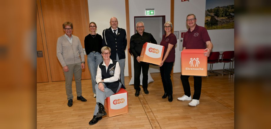 Gruppenfoto mit den Spielmannszügen aus Binningen und Illerich. Gruppenfoto mit den Spielmannszügen aus Binningen und Illerich. Auf dem Foto sind Männer und Frauen zu sehen. Bürgermeister Albert Jung und eine Frau halten eine größeren bunten Würfel mit Schriftzug evm in den Händen. Einen weiteren Würfel hält ein Mann und eine Frau sitzt vor der Grupp auf einem Würfel mit dem Schriftzug evm.