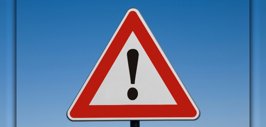 Ein Achtungsschild mit einem Ausrufezeichen vor einem hellblauen Himmel. Vor einem blauen Hintergrund, der den Himmel darstellen soll, ist ein dreieckiges Schild mit weißem und rotem Rand zu sehen. Das Schild ist ein Achtungsschild, in dem ein schwarzes Ausrufezeichen enthalten ist.