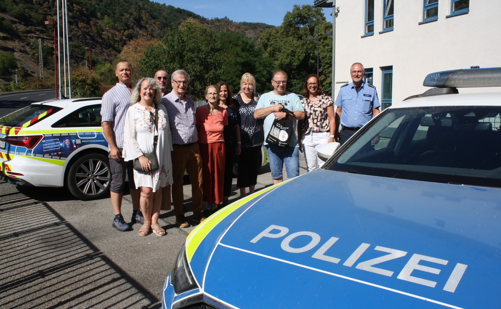 Eine Gruppe von Menschen steht vor zwei Polizeifahrzeugen vor der Polizeidienststelle Cochem.