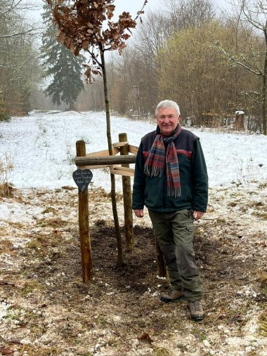Michael Fohl steht rechts von der gepflanzten Eiche, die als Erinnerungsbaum für ihn gepflanzt wurde. Michael Fohl steht rechts von der gepflanzten Eiche, die als Erinnerungsbaum für ihn gepflanzt wurde. Die Eiche steht auf einer Lichtung im Revier Hochpochten/Masburg. Es ist ein winterliches Bild und im Hintergrund liegt Schnee.
