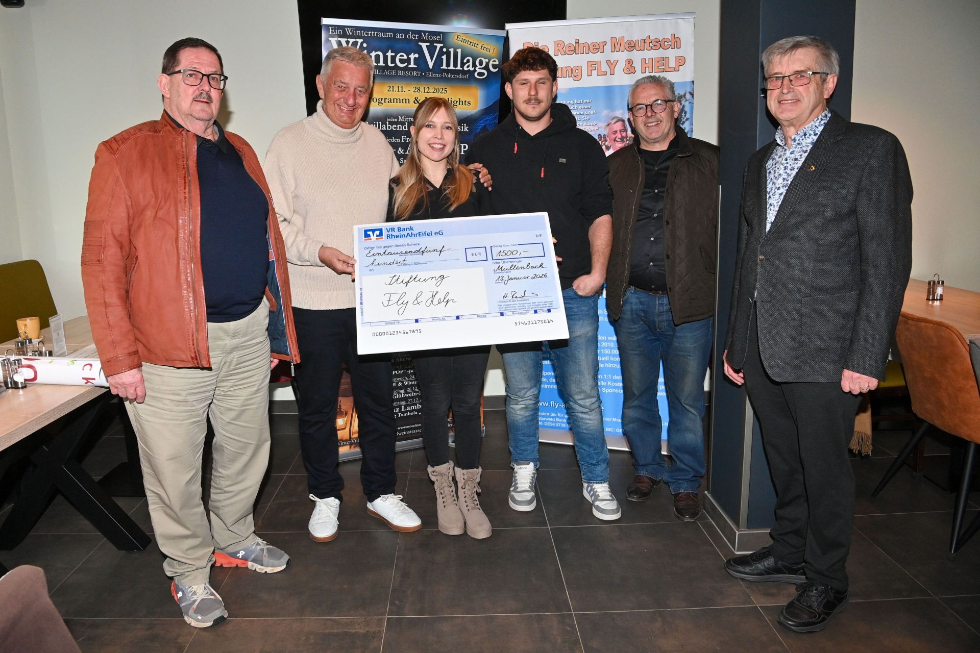 Auf dem Foto sind 6 Personen zu sehen. Eine Frau hält einen großen Scheck in der Hand, auf dem der Spendenbetrag in Höhe von 1.500 Euro steht. Die Menschen stehen vor zwei Roll-ups, die mit Werbung versehen sind.