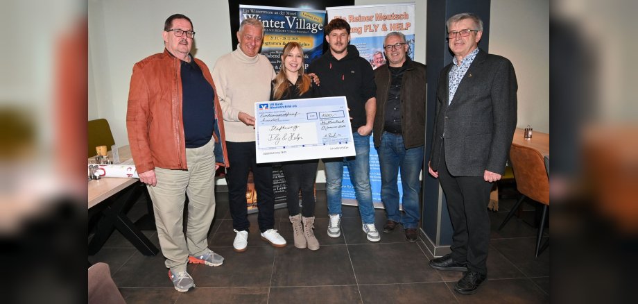 Auf dem Foto sind 6 Personen zu sehen. Eine Frau hält einen großen Scheck in der Hand, auf dem der Spendenbetrag in Höhe von 1.500 Euro steht. Die Menschen stehen vor zwei Roll-ups, die mit Werbung versehen sind.