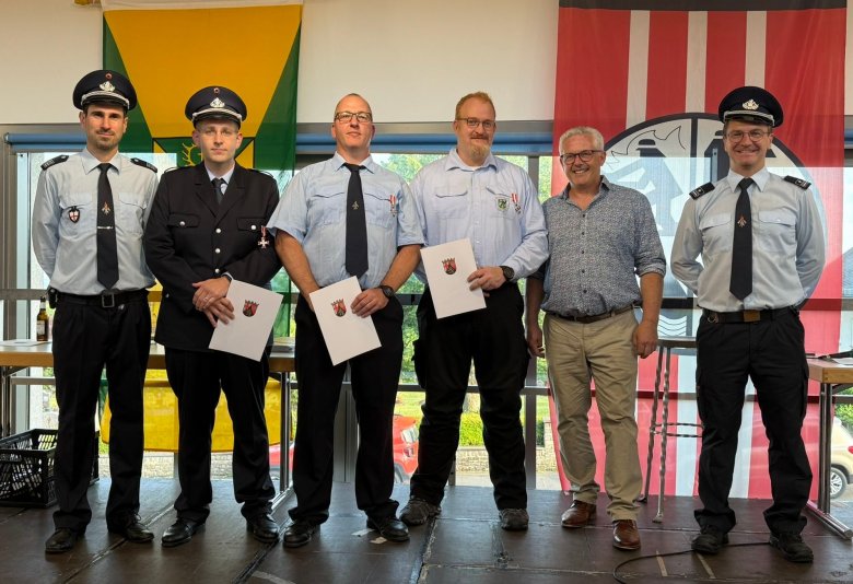 Gruppenfoto von den Ehrungen Gruppenfoto von den Ehrungen: Sechs Männer stehen bei der Ehrung auf der Bühne. Ein Mann hat eine Uniform an, drei Männer haben eine blaue Hose und ein hellblaues Hemd an, davon haben drei eine Krawatte an. Ein Mann hat eine beigefarbene Hose an und ein gemustertes Hemd. Das Foto hat einen feierlichen Charakter.
