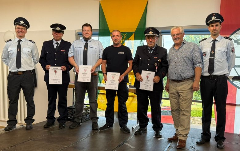 Gruppenfoto der ausgeschiedenen Wehrleiter Gruppenfoto der ausgeschiedenen Wehrleiter: Sieben Männer stehen bei der Verabschiedung auf der Bühne. Zwei Männer haben eine Uniform an, drei Männer haben eine blaue Hose und ein hellblaues Hemd mit Krawatte an, davon haben zwei auch eine Schirmmütze an. Ein Mann hat eine blaue Hose und ein blaues T-Shirt an. Ein weiterer Mann hat eine beigefarbene Hose und ein gemustertes Hemd an. Das Foto hat einen feierlichen Charakter.