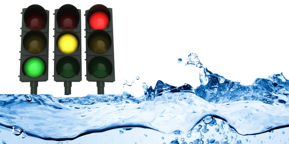 Das Bild zeigt drei Ampeln mit jeweils unterschiedlichen Lichtsignalen: grün, gelb und rot. Im Vordergrund ist eine dynamische Wasseroberfläche mit spritzenden Wellen zu sehen. Der Hintergrund ist weiß und klar.