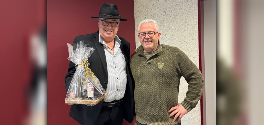 Hans-Günter Labonte und Bürgermeister Albert Jung Hans-Günter Labonte und Bürgermeister Albert Jung stehen stehen gemeinsam vor einer rot-weißen Wand. Herr Labonte hält ein Präsent in der Hand.