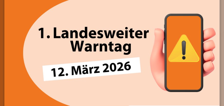 Hinweis zum landesweiten Warntag am 12. März 2026. Das Foto  zeigt auf der rechten Seite eine Hand, die ein Smartphone hält, auf dem ein gelbes Dreieck und ein Fragezeichen abgebildet sind. Auf der linken Seite steht "1. Landesweiter Wantag" und das Datum 12. März 2026.