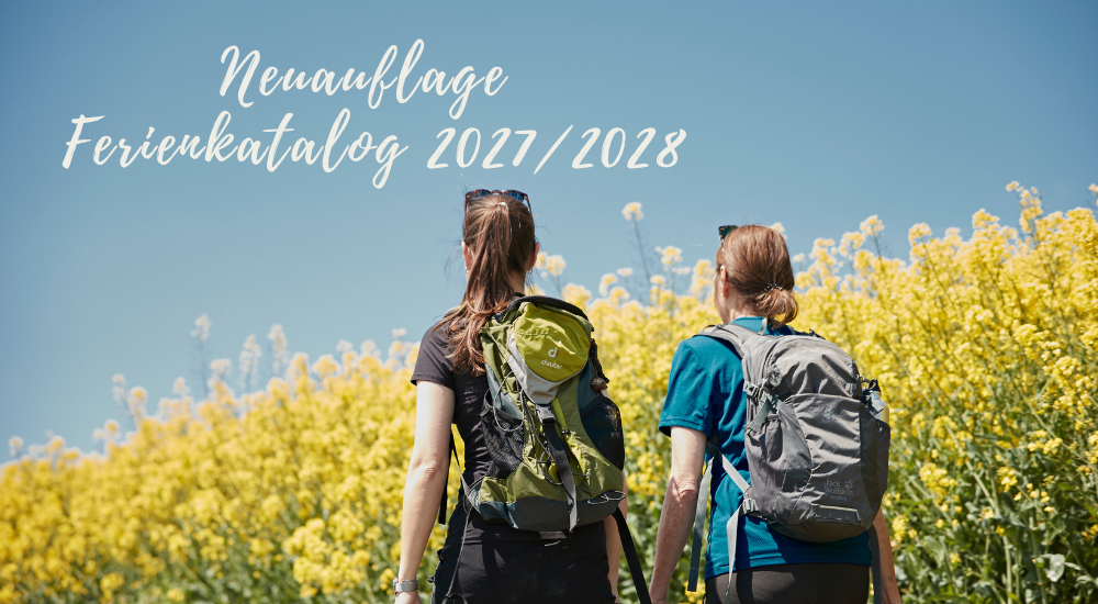 Zwei Wanderinnen mit Rucksäcken gehen durch eine gelb blühende Landschaft unter blauem Himmel. Im Bild steht: „Neuauflage Ferienkatalog 2027/2028“