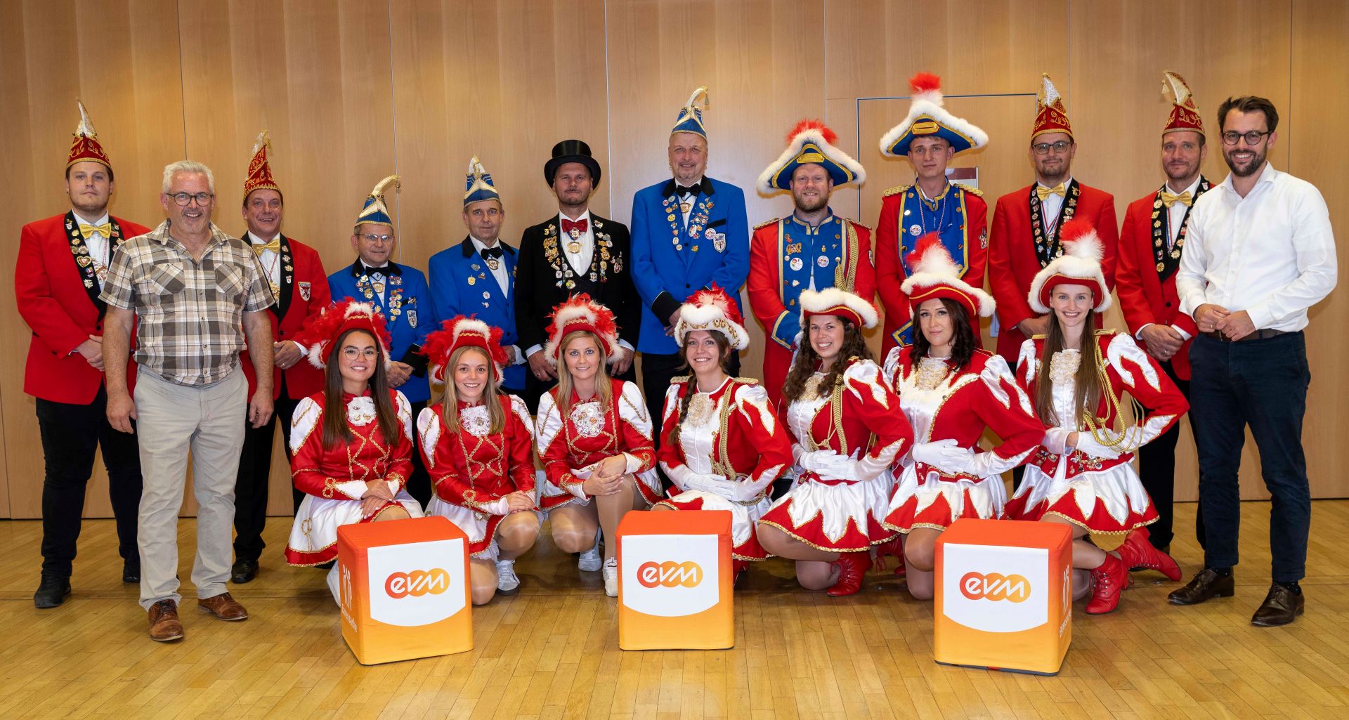 Gruppenfoto mit Bürgermeister Albert Jung, Hubertus Hacke-Dietze, und Vertretern der Karnevalsvereine Müllenbach und Kaisersesch. Die Vertreter der Karnevalsgesellschaften tragen festliche rote und blaue Uniformen. Im Vordergrund stehen drei orangefarbene Würfel.