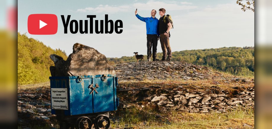 Digi-Pfad Kaulenbachtal Zwei Wanderer mit Hund stehen auf einer Halde neben einem alten Förderwagen; oben links ist das YouTube-Logo zu sehen.