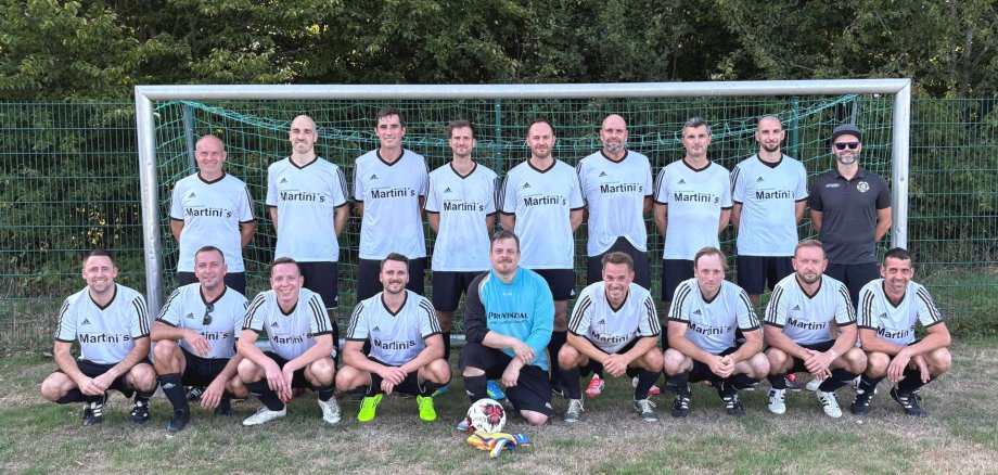 Die Spieler des TuS Kaisersesch AH freuten sich riesig über den Pokalgewinn. Fußballmannschaft in weißen Trikots posiert gemeinsam mit einem Torwart im blauen Trikot und einem Trainer vor einem Fußballtor; vor der Gruppe liegt ein Fußball auf dem Rasen.