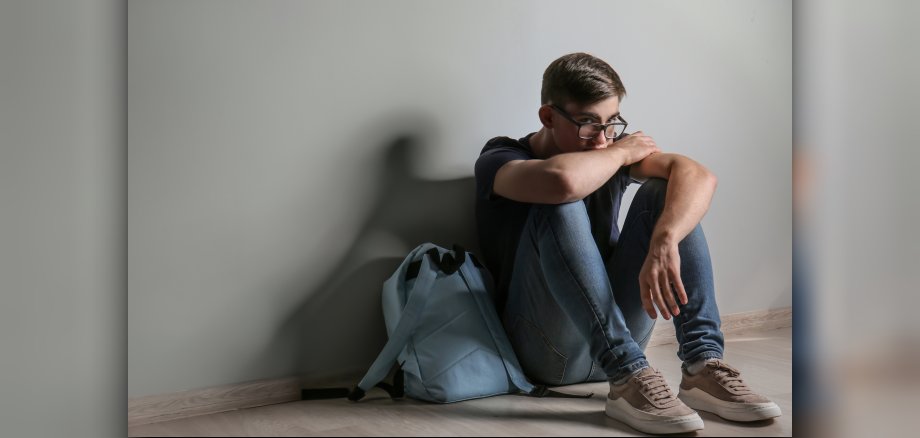 Ein junger Mann sitzt auf dem Boden eines Zimmers.